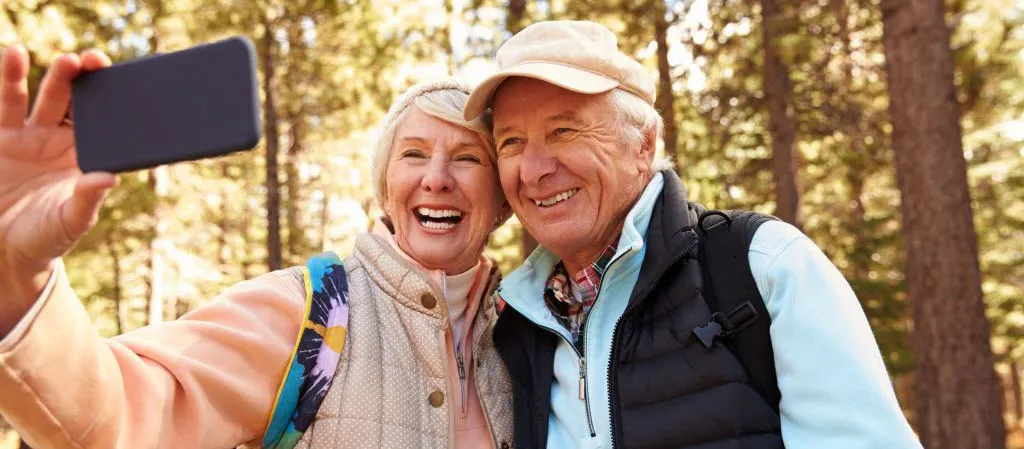 Retired couple smiling and taking a picture of themselves in an outdoor setting. 